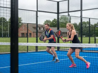 Two players at the net during a padel match, seen through the court glass