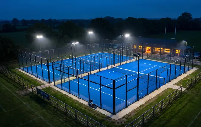 Four floodlit padel courts at dusk, with the clubhouse lit behind them